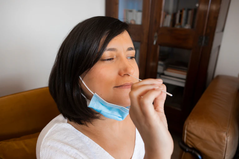 Woman taking own nasal swab with face mask around neck