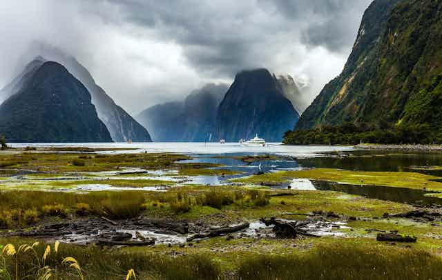 Natural landscape, with mounatins and tourist boats in a fiord, Fiordland National Park in New Zealand.
