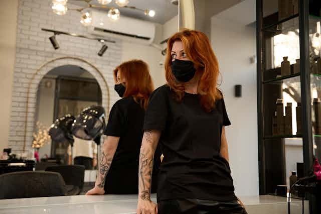 Hairdresser in a mask looks towards the door.
