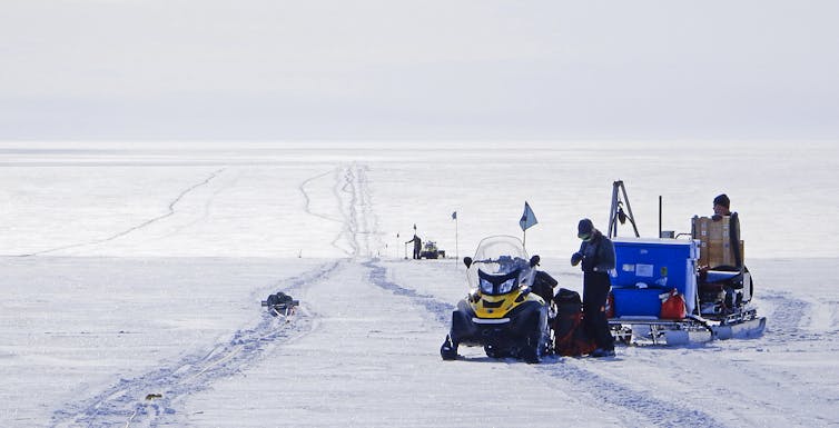 Scientists surveying over Antarctica's ice sheet and snow with skidoo and sleds.