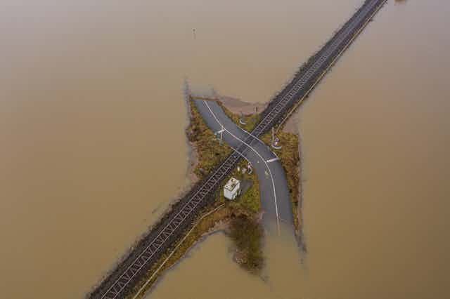 A road disappears into flooded water and a railway intersects with it.