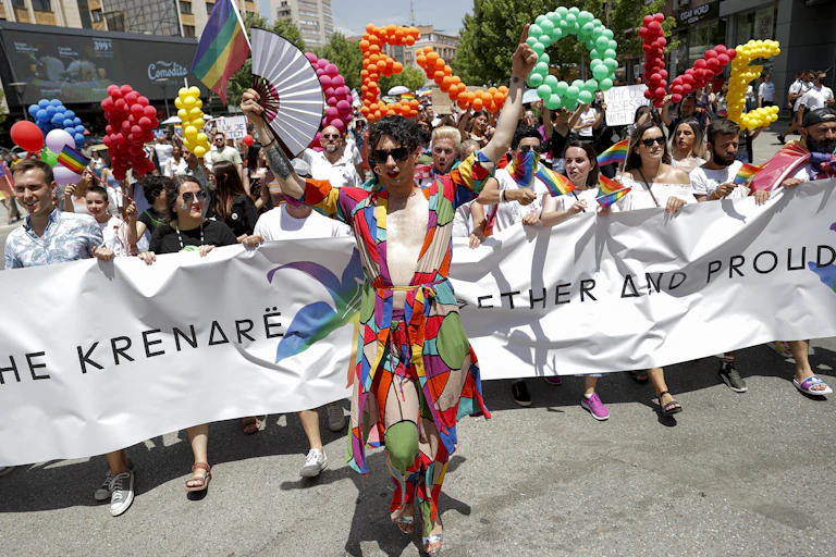 Gay Pride parade in Kosovo, with man in a robe walking in front of a many others holding a banner