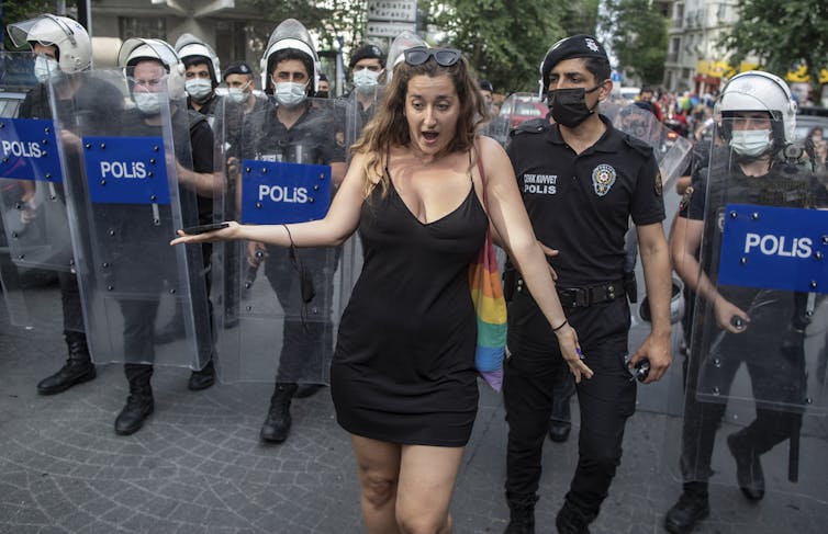 Woman with a gay pride bag being escorted by police with riot shields in Istanbul