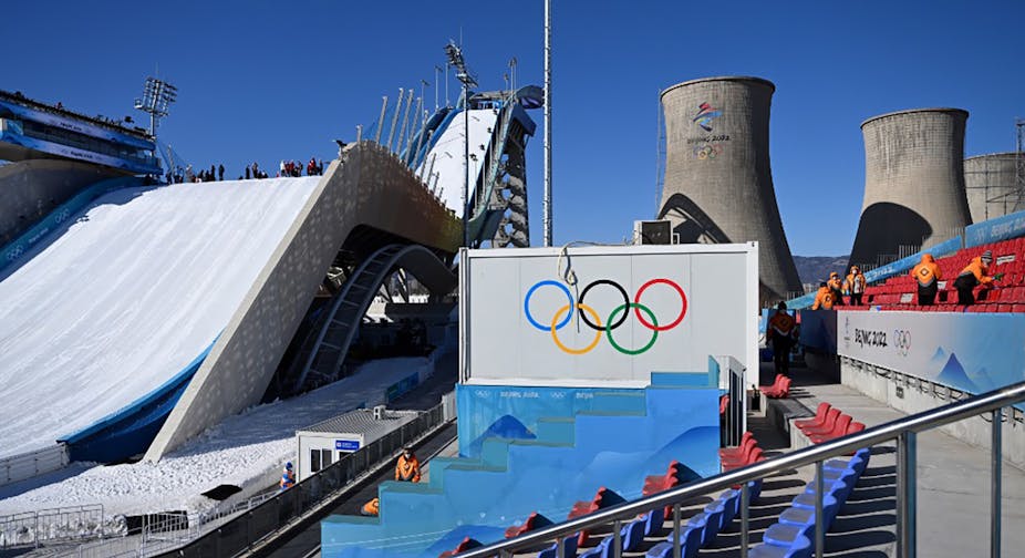 En arrière-plan de la piste de Big Air, derrière un panneau avec les anneaux olympique, on peut voir des cheminées de refroidissement de l'ancienne usine d'acier. 