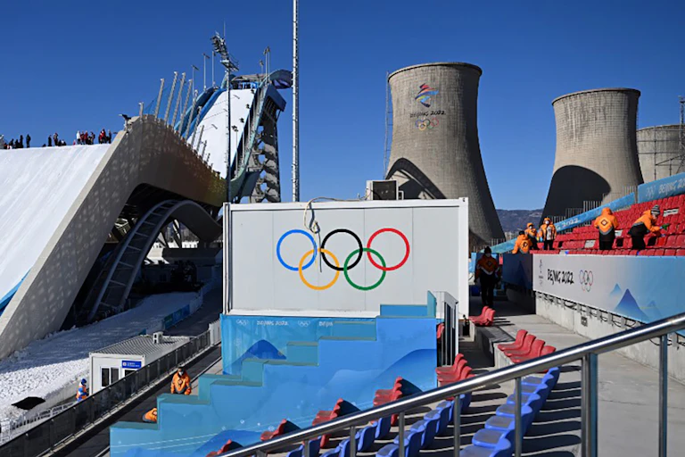 En arrière-plan de la piste de Big Air, derrière un panneau avec les anneaux olympique, on peut voir des cheminées de refroidissement de l'ancienne usine d'acier.
