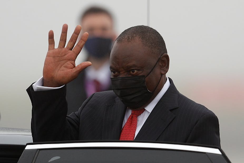 Man wearing suit and tie and face mask raises his right hand