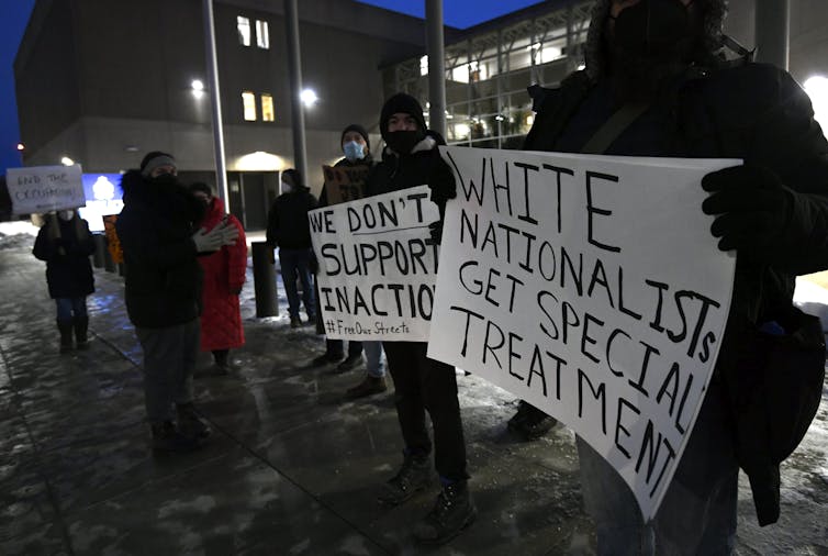 Protesters hold signs as they stand on a darkened street. One reads 'white nationalists get special treatment'