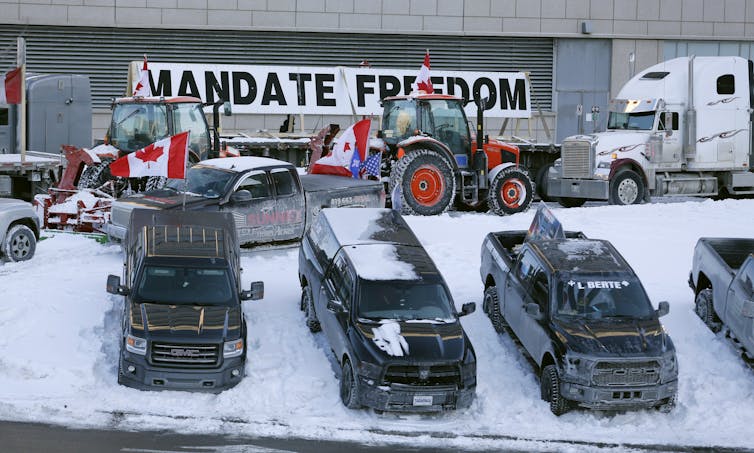 Trucks sit parked with tractors in front of a giant sign that reads 'MANDATE FREEDOM'