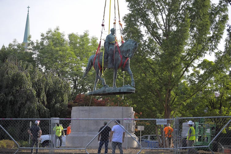 Trabajadores de la construcción usan cadenas resistentes para quitar una estatua.