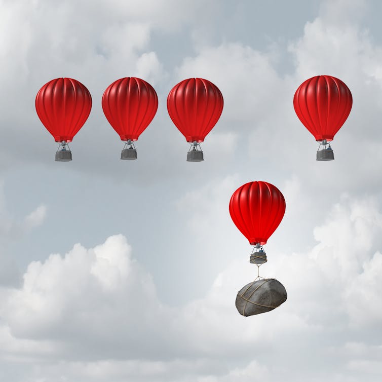 Illustration of five red hot-air balloons rising into the air, with one held back by a large rock tied to it.