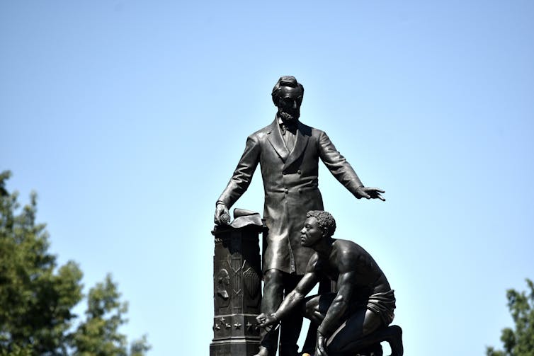 A statue of a man standing near another man on his knees.