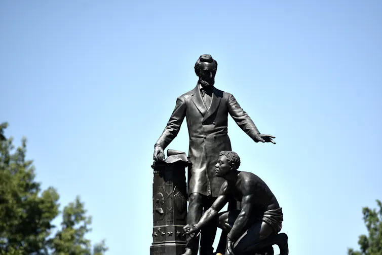 A statue of a man standing near another man on his knees.