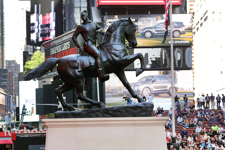 A statue of a black man with dred locks and wearing a hoodie sweatshirt is sitting atop a horse.