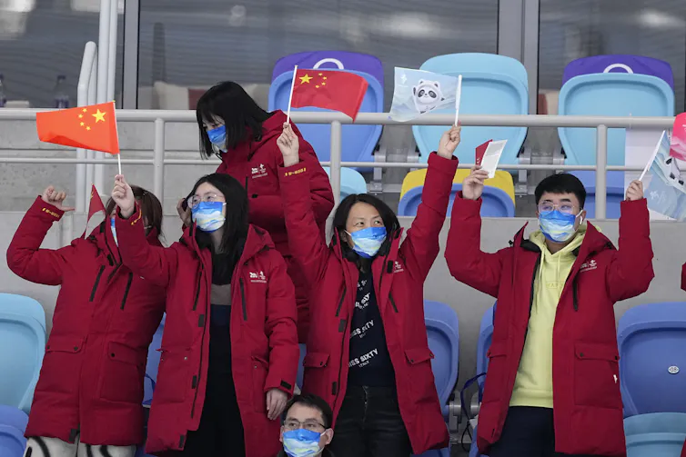 Four people in long, red winter coats wave Chinese flags