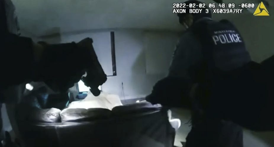 A grainy bodycam image shoes two officers walking into a dimly-lit room.