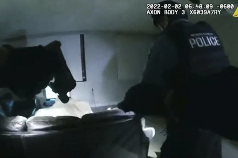 A grainy bodycam image shoes two officers walking into a dimly-lit room.