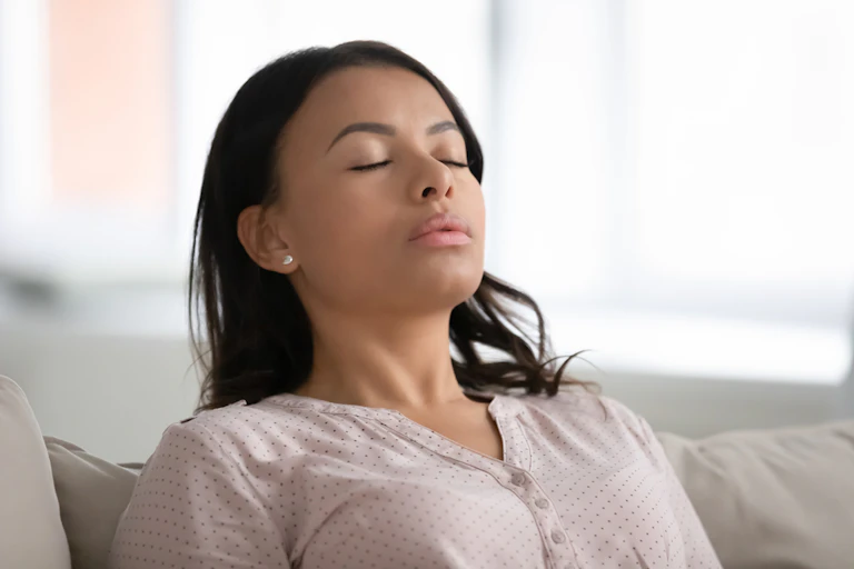 Woman sitting on sofa, eyes shut, exhaling