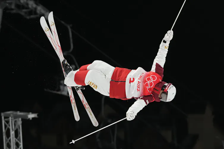 Skier does aerial trick mid-air, with one arm extended upwards.