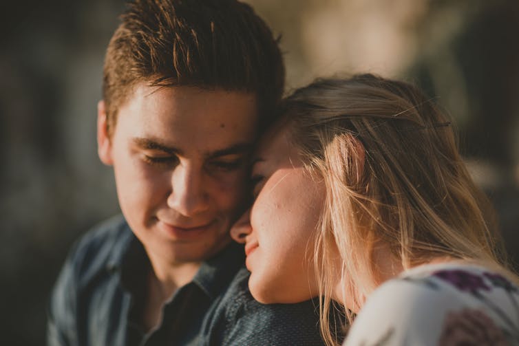 A young heterosexual couple cuddle in to each other.