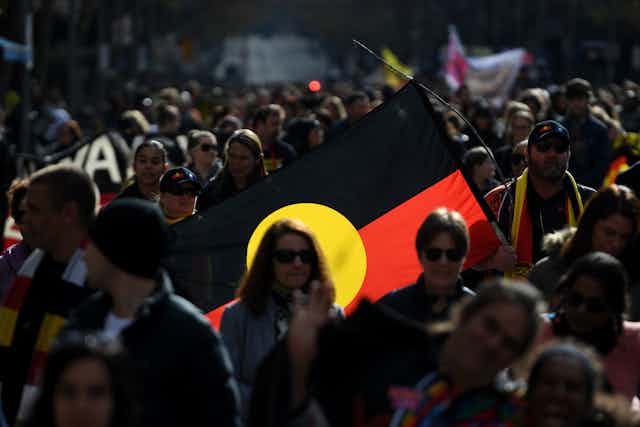 People in a NAIDOC march with an Aboriginal flag.