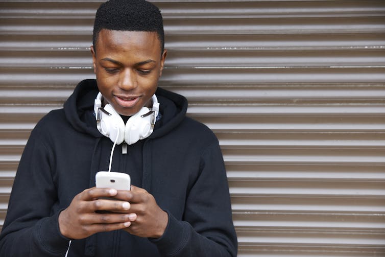 Young African-Australian boy looks at his phone, texting.