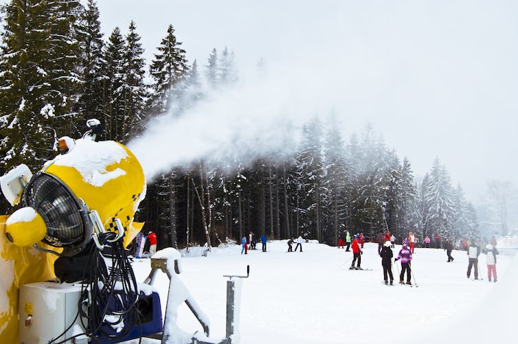 Snowgun shoots artificial snow towards skiers.