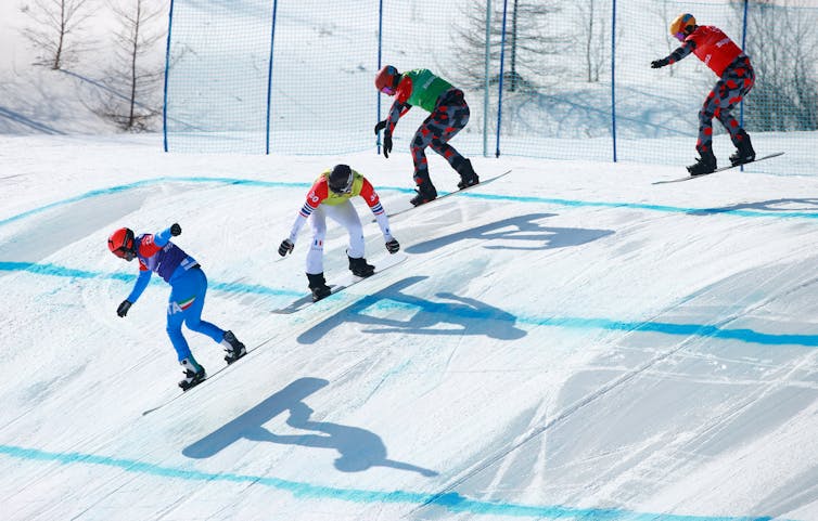 Four snowboarders crest a snow-covered hill.