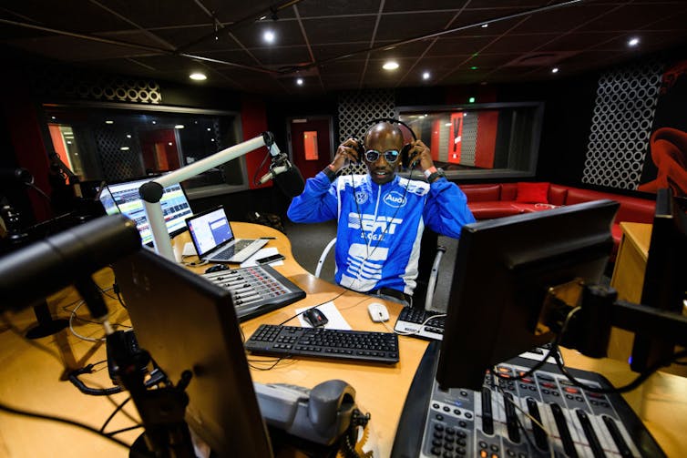 A young man in bright blue shirt sits in a high tech radio studio.