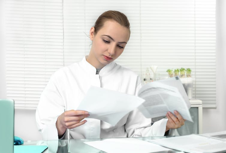 Young woman wearing a lab coat reviews some research papers.