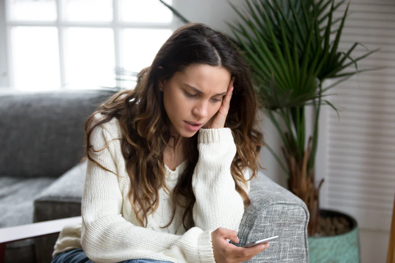 A young woman looks at her smarphone, appears unsettled.