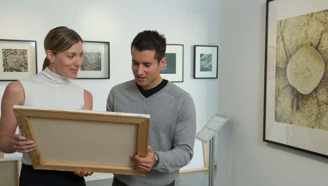 Two white curators examine a painting.