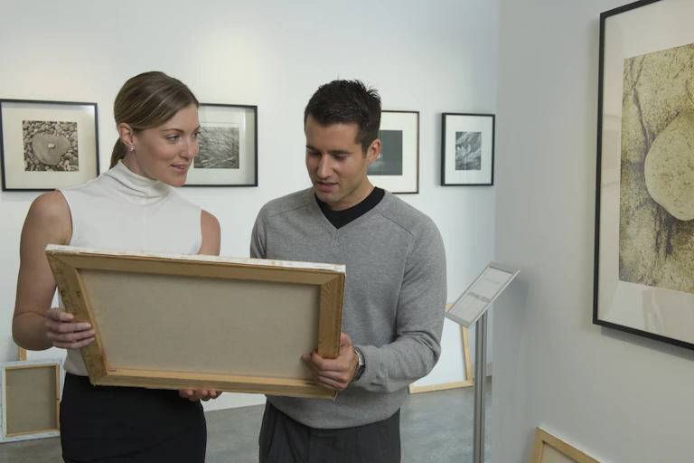 Two white curators examine a painting.