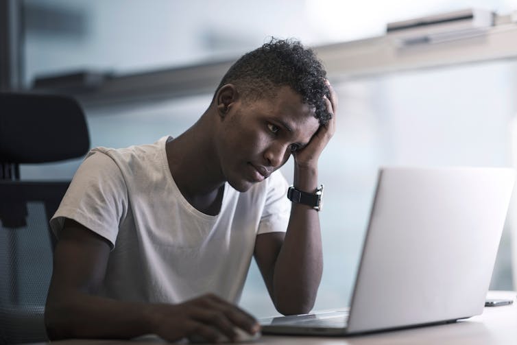 A young man sits in front of a laptop.