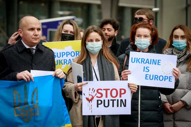 People gather outside the European Parliament for a rally in support of Ukraine's sovereignty holding anti-Putin signs in English.
