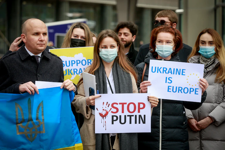 People gather outside the European Parliament for a rally in support of Ukraine's sovereignty holding anti-Putin signs in English.