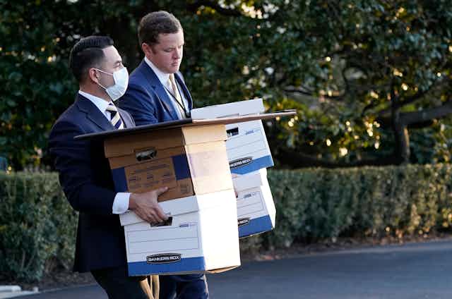 Two White House staffers in suits carry boxes