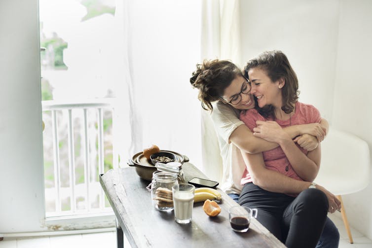 Two women cuddle in a kitchen.