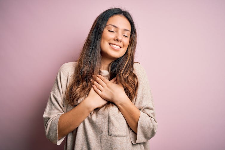 A woman clutches her heart while smiling.