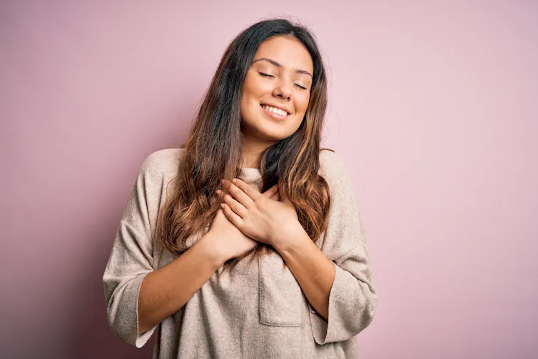 A woman clutches her heart while smiling.