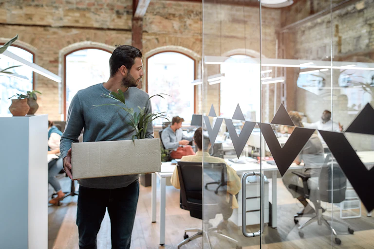 Young man carrying box of belongings leaves office