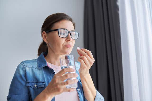 Woman taking pill with glass of water at home