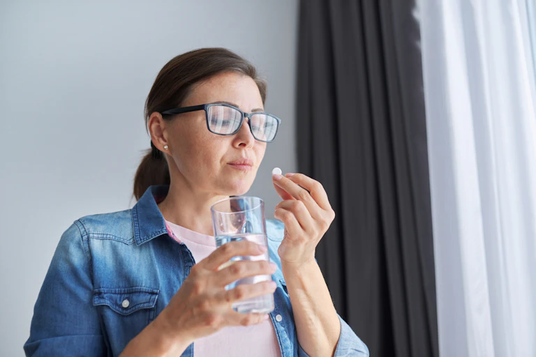 Woman taking pill with glass of water at home