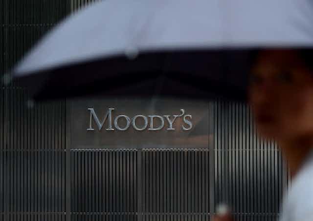 A view of a building from the street with a sign in the building that reads 'Moody's' and a person carrying an umbrella in the foreground.