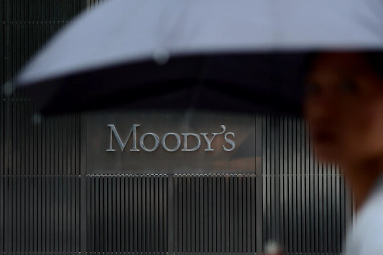 A view of a building from the street with a sign in the building that reads 'Moody's' and a person carrying an umbrella in the foreground.