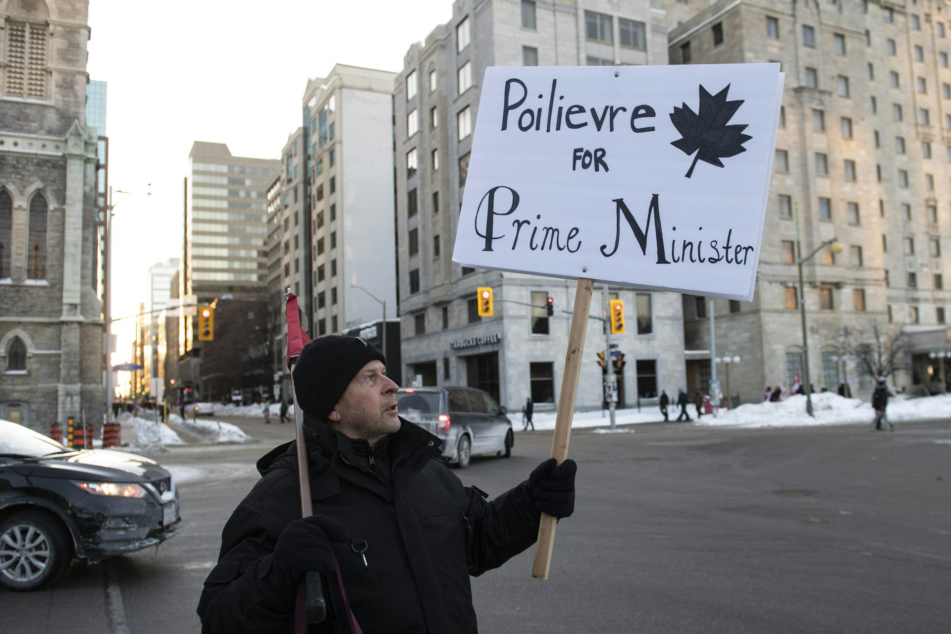 A man holds a sign that reads Pierre Piolievre for prime minister on a city street.
