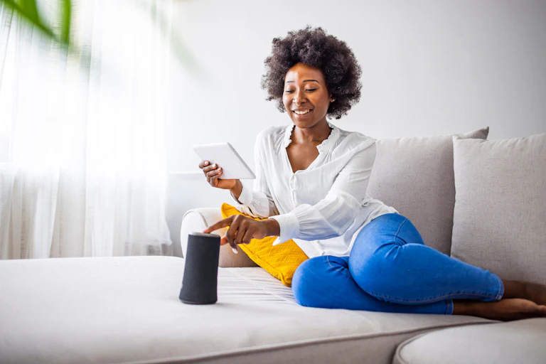 A woman on the couch holding a tablet and touching a smart device.