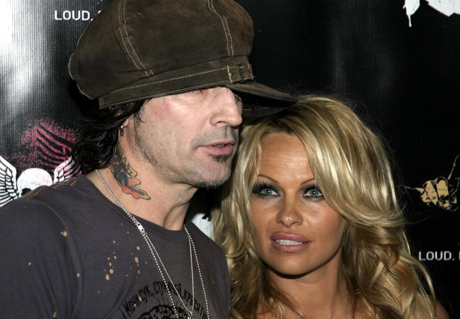 Photo of Tommy Lee and Pamela Anderson at an event. Tommy is wearing a brown cap pulled over his eyes