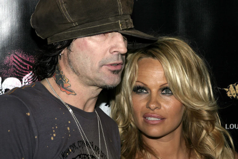 Photo of Tommy Lee and Pamela Anderson at an event. Tommy is wearing a brown cap pulled over his eyes