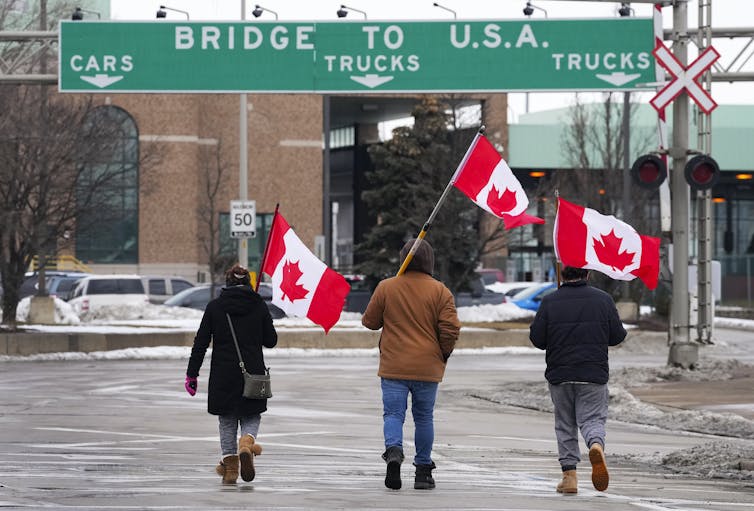 Three protesters carrying Canadian flags at the Ambassador Bridge.