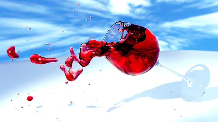 A glass of wine tipping over against a blue sky